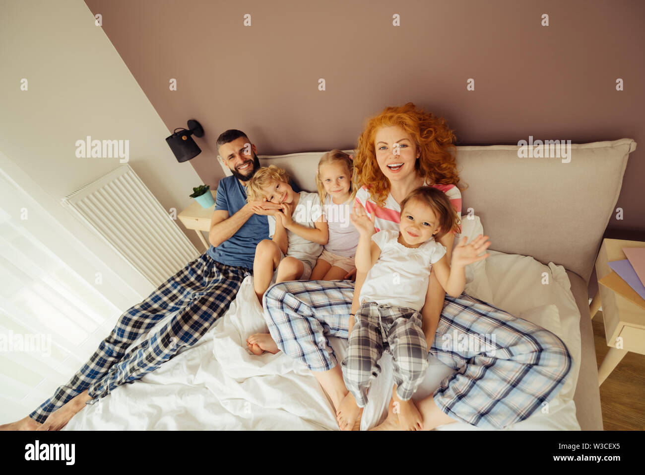 Happiness and fun. Positive joyful family sitting together on the bed while enjoying their time Stock Photo