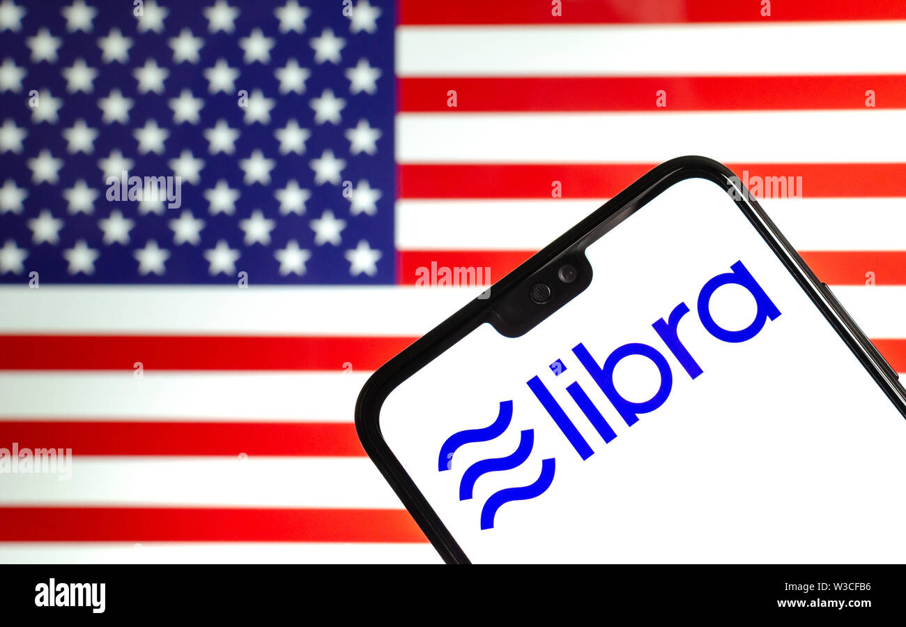 Facebook Libra crypto currency logo on the smartphone and blurred flag of the USA at a laptop screen on the background. Conceptual photo. Stock Photo