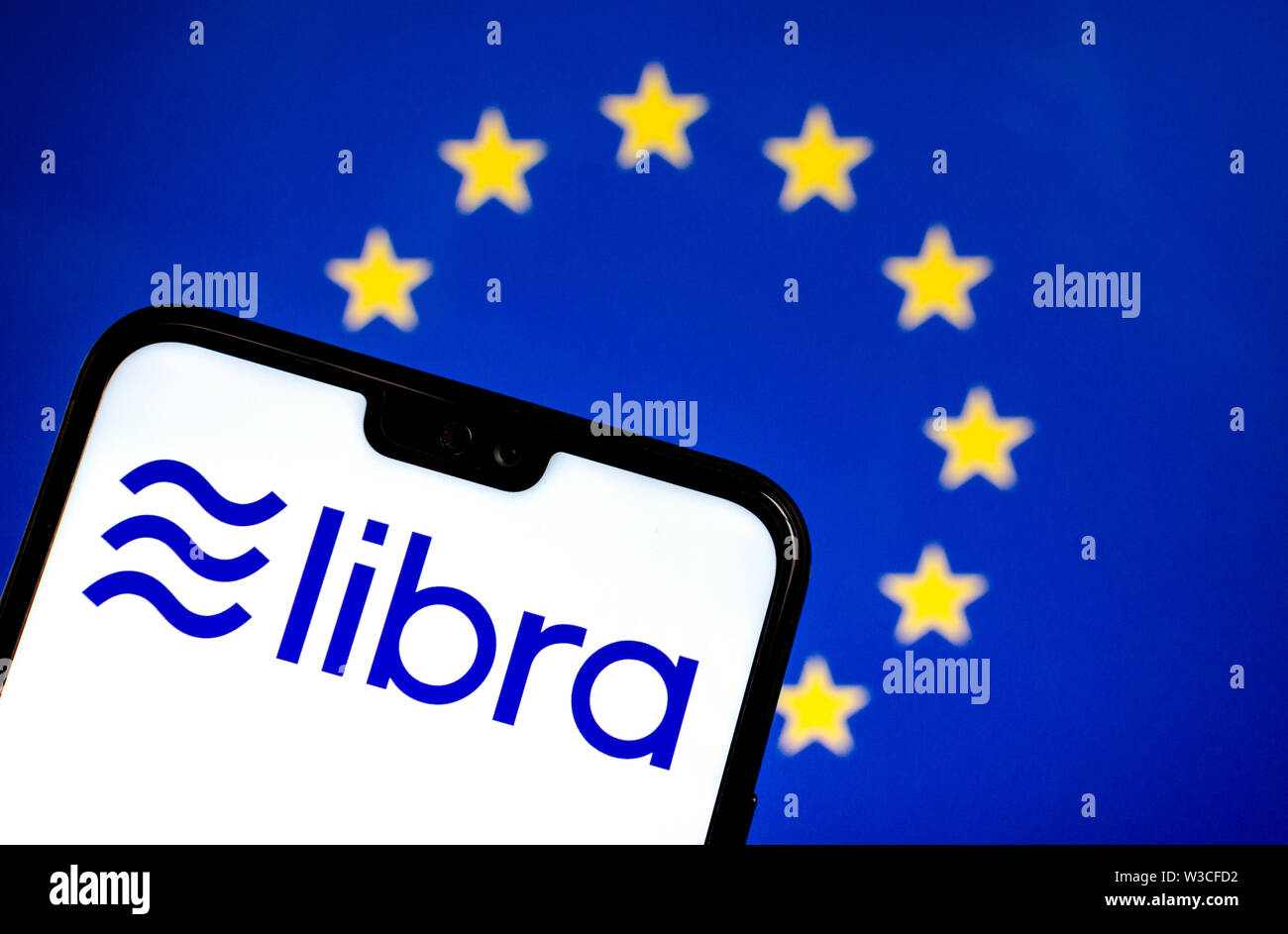 Facebook Libra crypto currency logo on the smartphone and blurred flag of  EU at a laptop screen on the background. Conceptual photo. Stock Photo