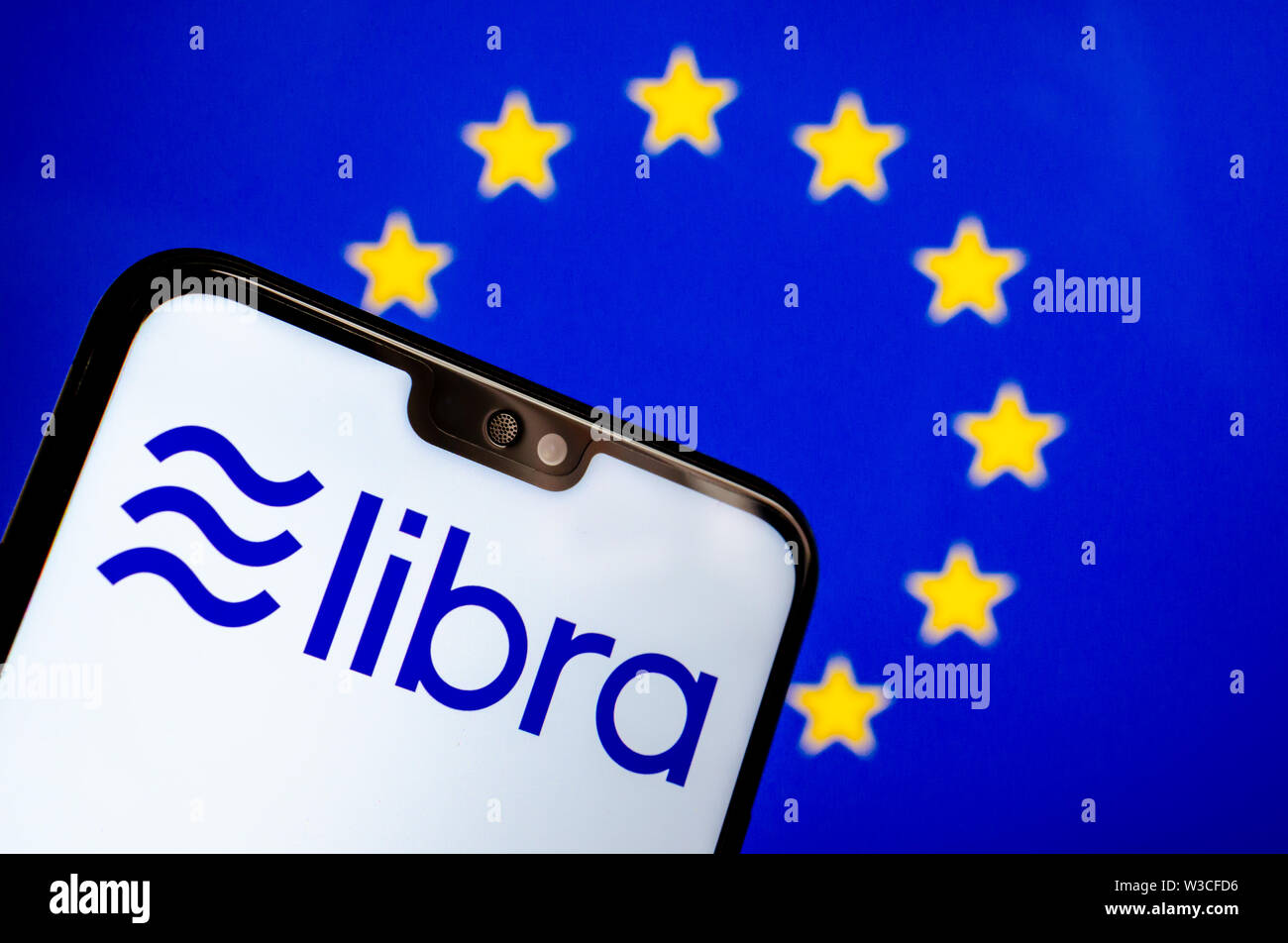 Facebook Libra crypto currency logo on the smartphone and blurred flag of  EU at a laptop screen on the background. Conceptual photo. Stock Photo