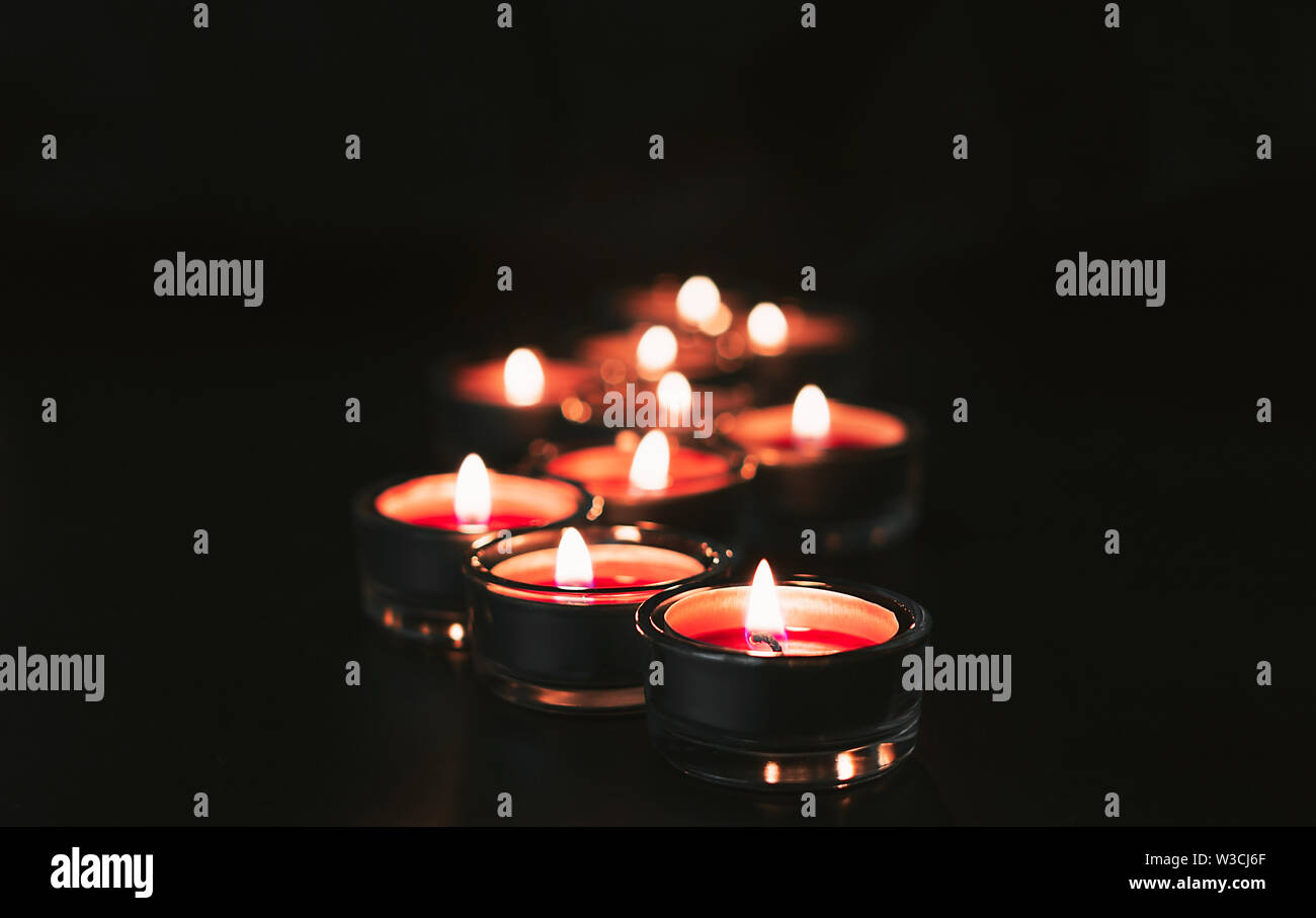 Many red candles lit in the dark with bokeh. Dark and moody feel. Close ...
