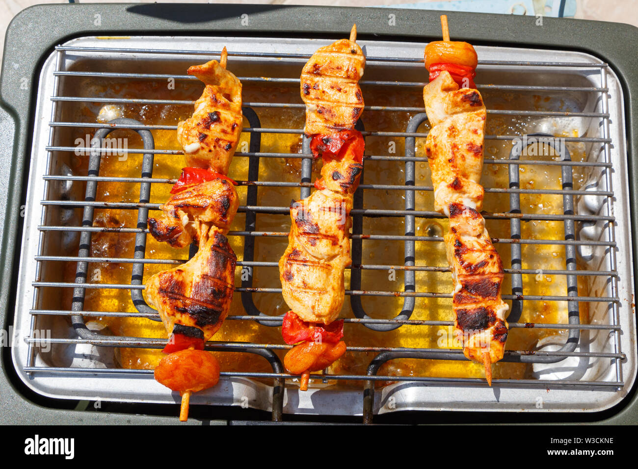 Three marinated chicken brochette on the grid of an electric barbecue Stock Photo