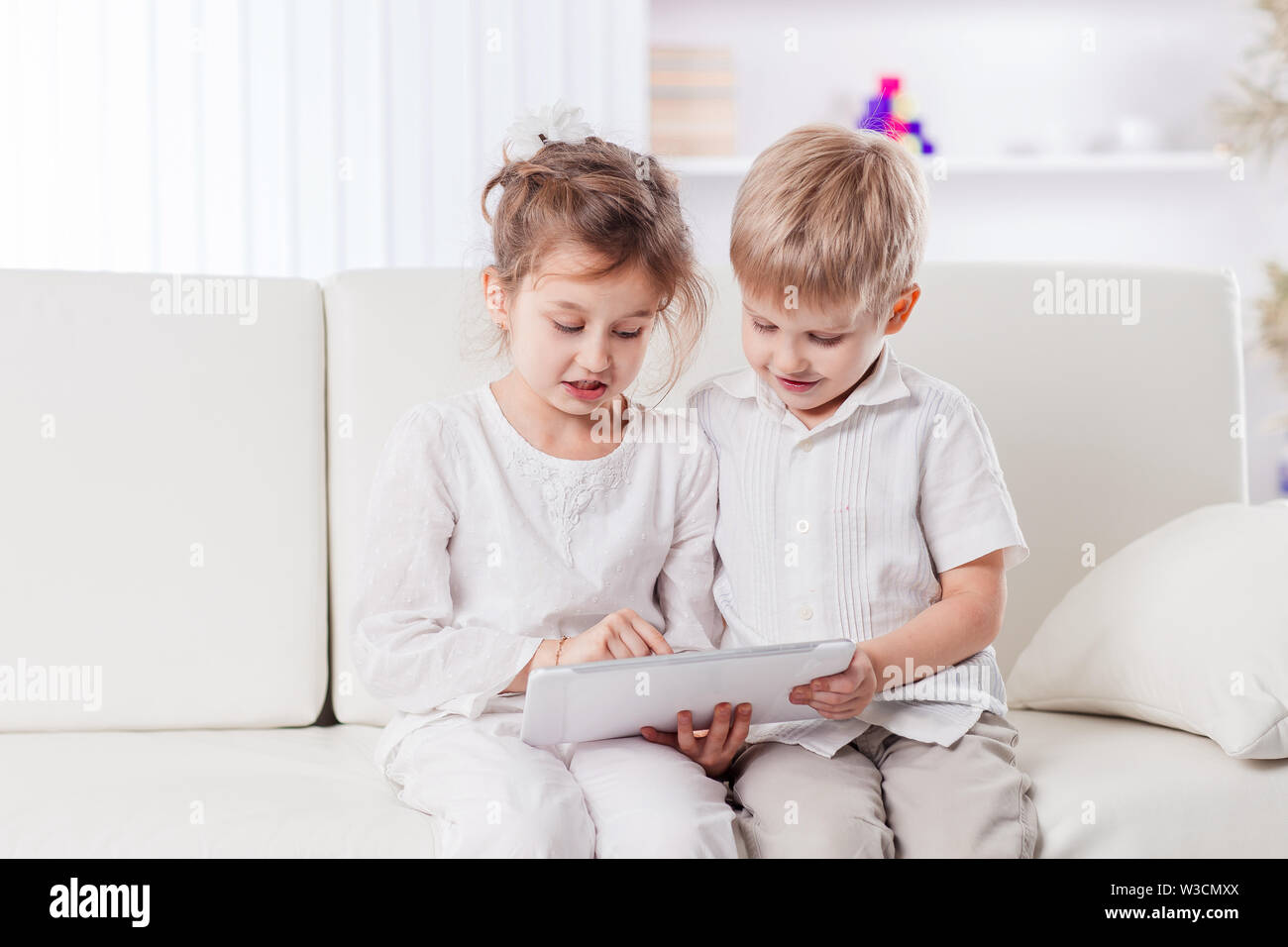 brother and sister with digital tablet sitting on sofa in living room ...