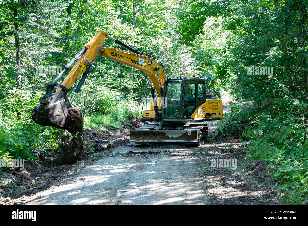 A SANY track hoe excavator clearing the ditches on an Adirondack Mountains, NY USA, forest logging road. Stock Photo