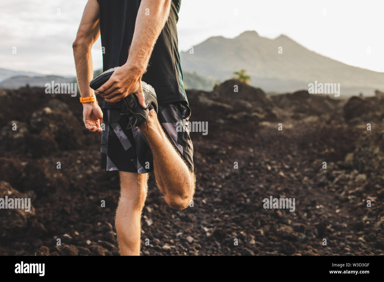 Runner stretching leg and feet and preparing for trail running outdoors. Active and healthy lifestyle concept. Mountain view on background. Stock Photo