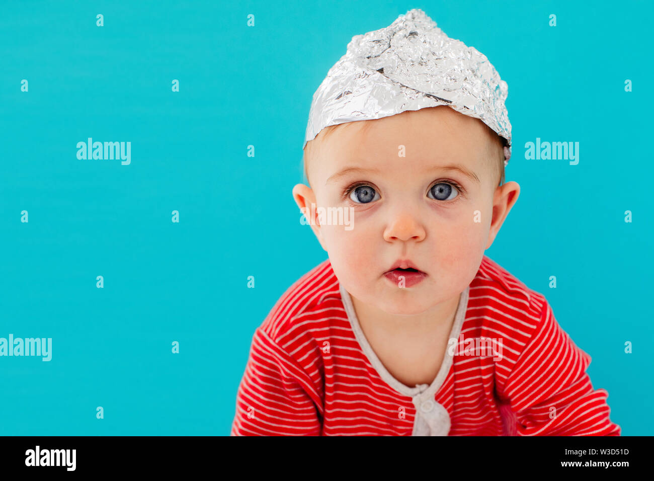Baby in a foil hat sits on a blue background Stock Photo