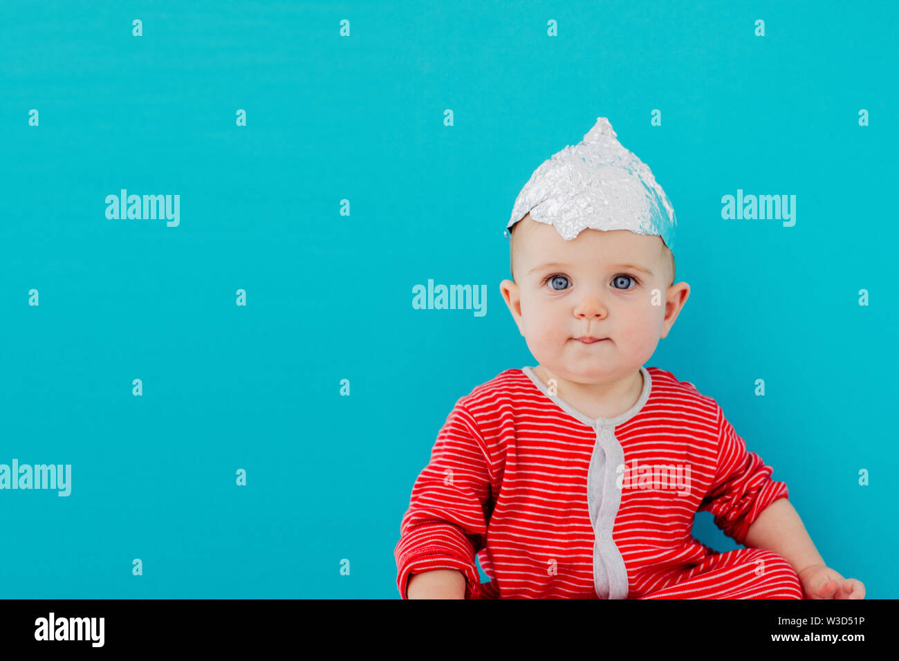 Baby in a foil hat sits on a blue background Stock Photo