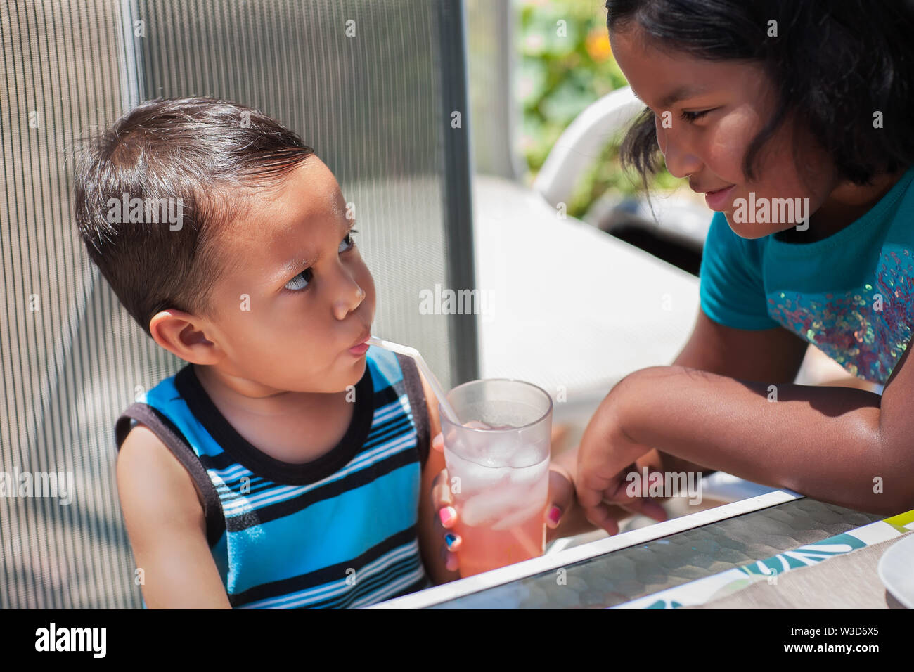Big sister is holding a pink lemonade drink for his little brother to drink from a straw during summertime. Stock Photo