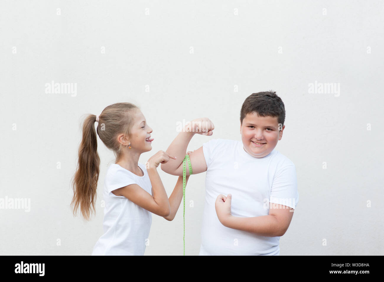 thin little girl in white t-shirt measuring muscle of fat small boy and tease him Stock Photo
