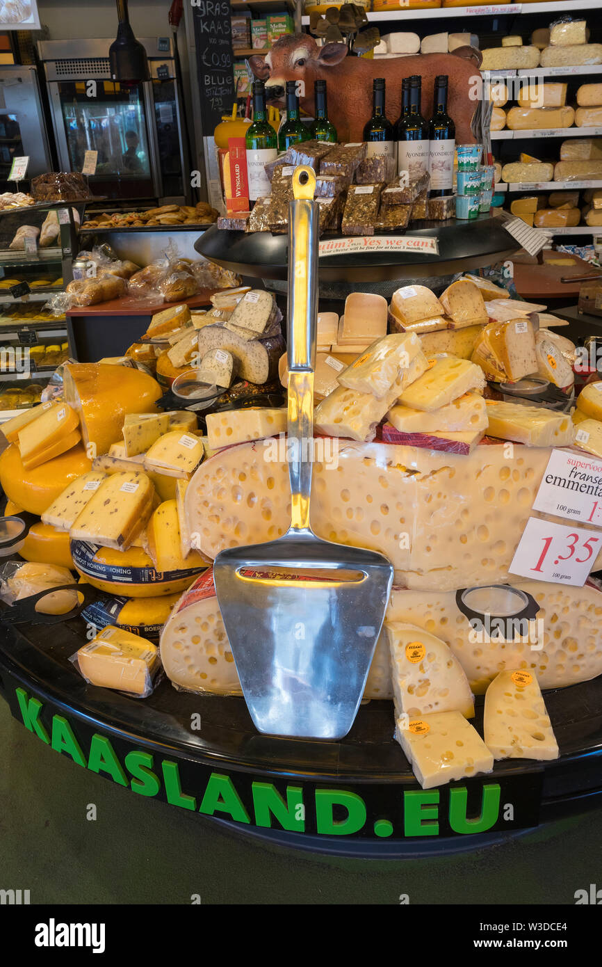 Amsterdam, Holland - June 22, 2019: Display of a variety of cheese in a cheese shop and a giant cheese slicer Stock Photo