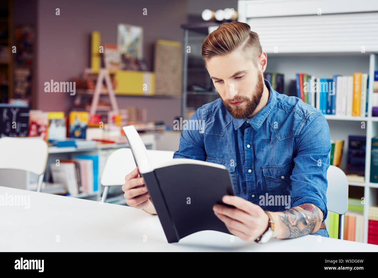 Concentrated handsome young man reading textbook while sitting in library Stock Photo