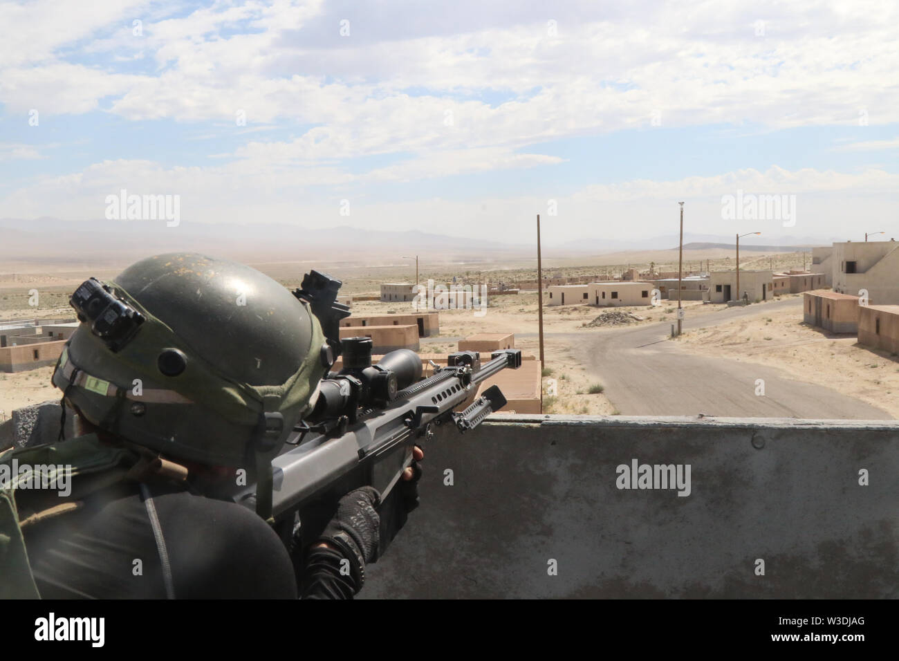An 11th Armored Cavalry Regiment Trooper surveys the battlefield with a simulated Barrett M107 .50 caliber Sniper Rifle in the city of Razish, National Training Center, Fort Irwin, Calif., on July 12th, 2019. This mission tested the 30th ABCT’s ability to react under fire while maneuvering through a controlled city.  (U.S. Army photo by PV2 James Newsome) Stock Photo