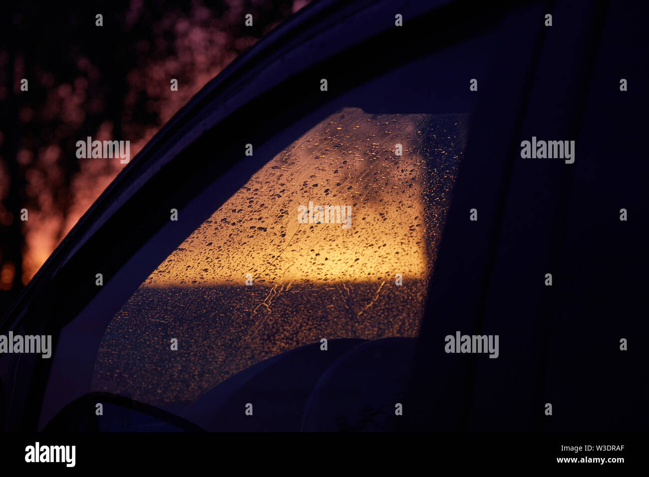 Car windshield covered with raindrops against sunset Stock Photo