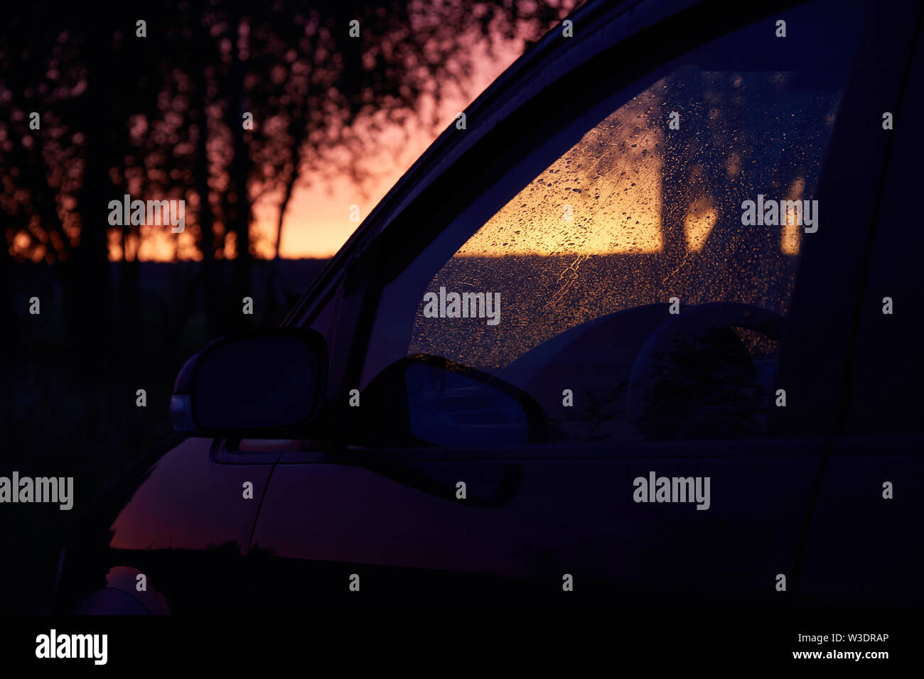 Car windshield covered with raindrops against sunset Stock Photo