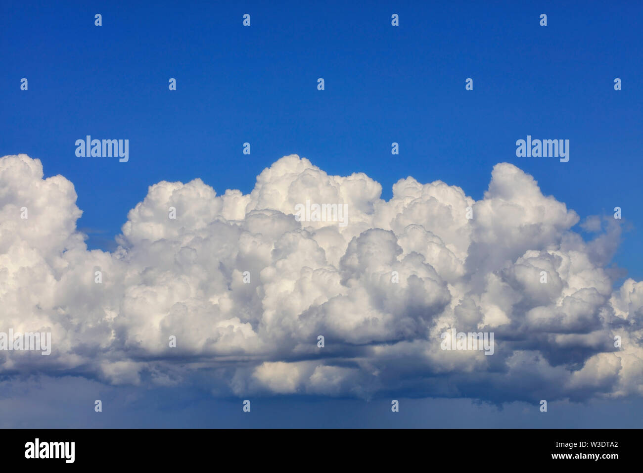 In the blue sky a white-gray fluffy cloud gradually gathering rain. Stock Photo