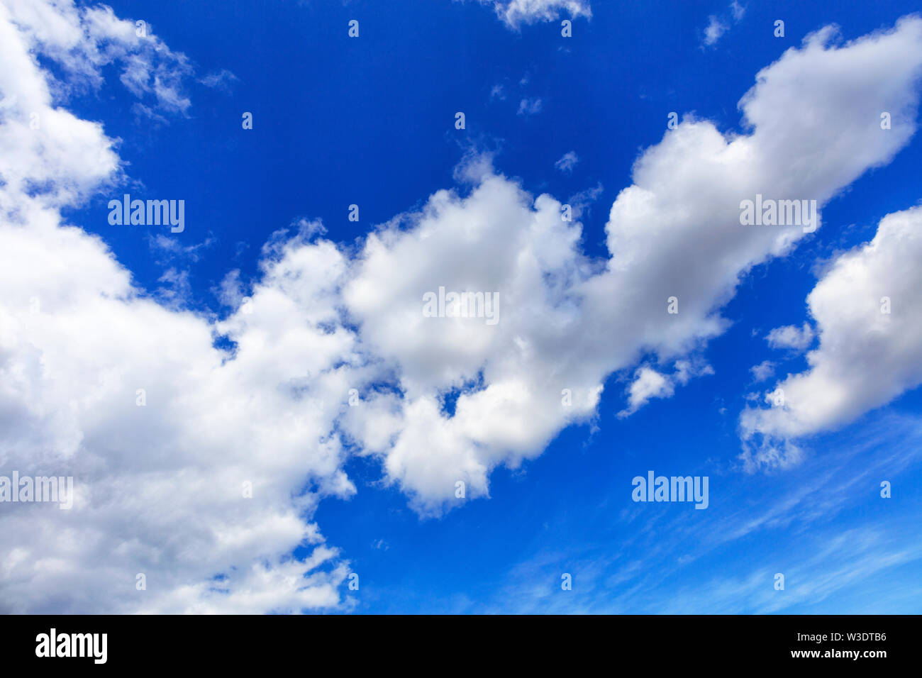 In the blue sky white fluffy clouds strive skyward, dividing the picture diagonally. Stock Photo