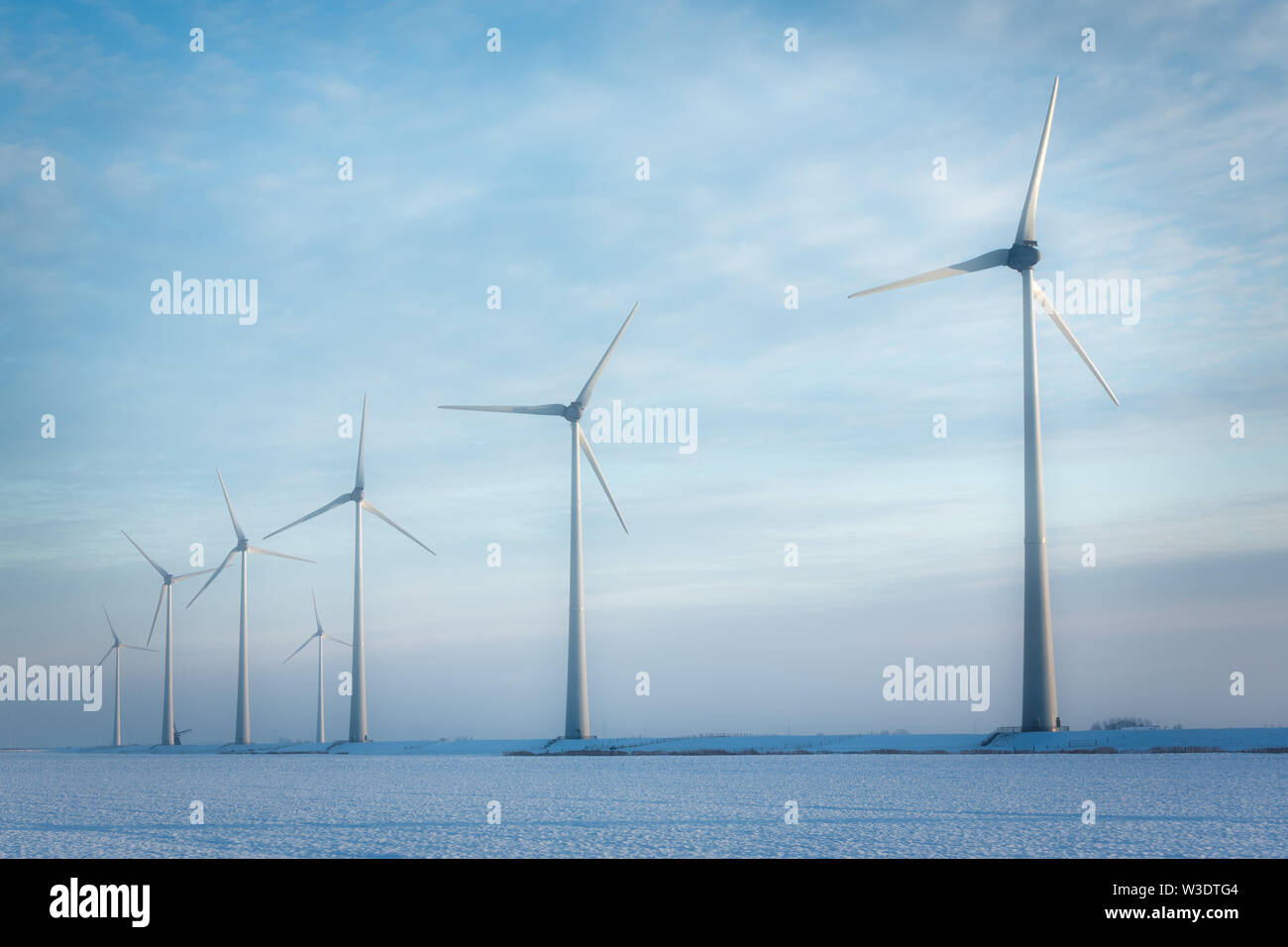 Windmills in a white winter landscape with snow producing green and sustainable energy to reduce global warming - Eemshaven, Groningen, The Netherland Stock Photo