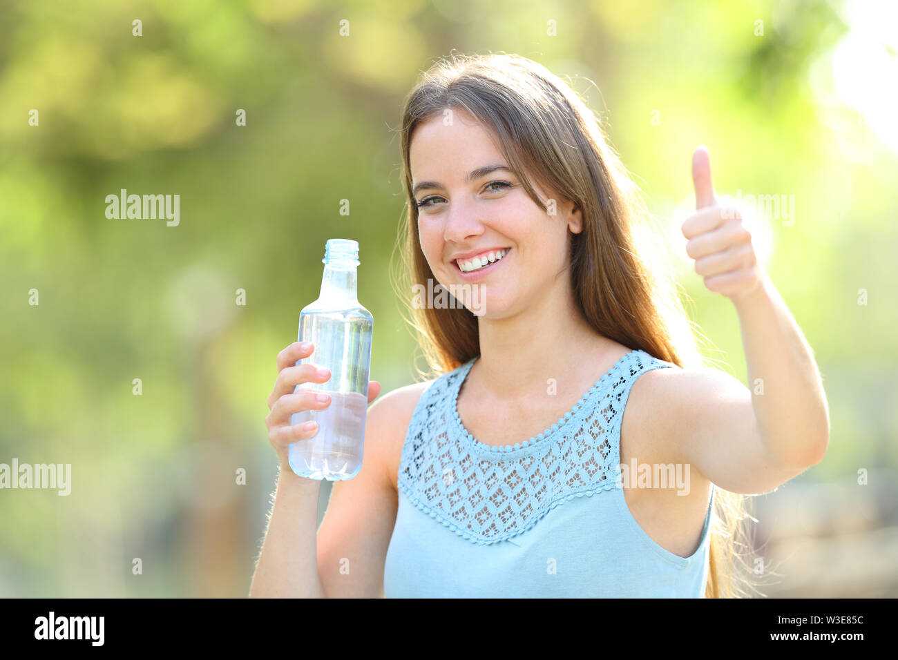 Happy woman holding a water bottle with thumbs up in a park with a ...