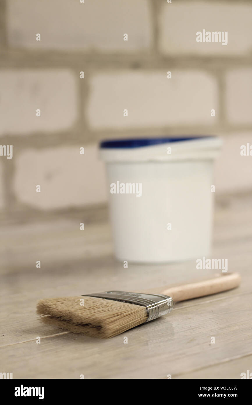 A paint brush is next to a plastic paint bucket with a blue lid on an old white vintage wooden board. Brick wall in the background. Place for text or Stock Photo