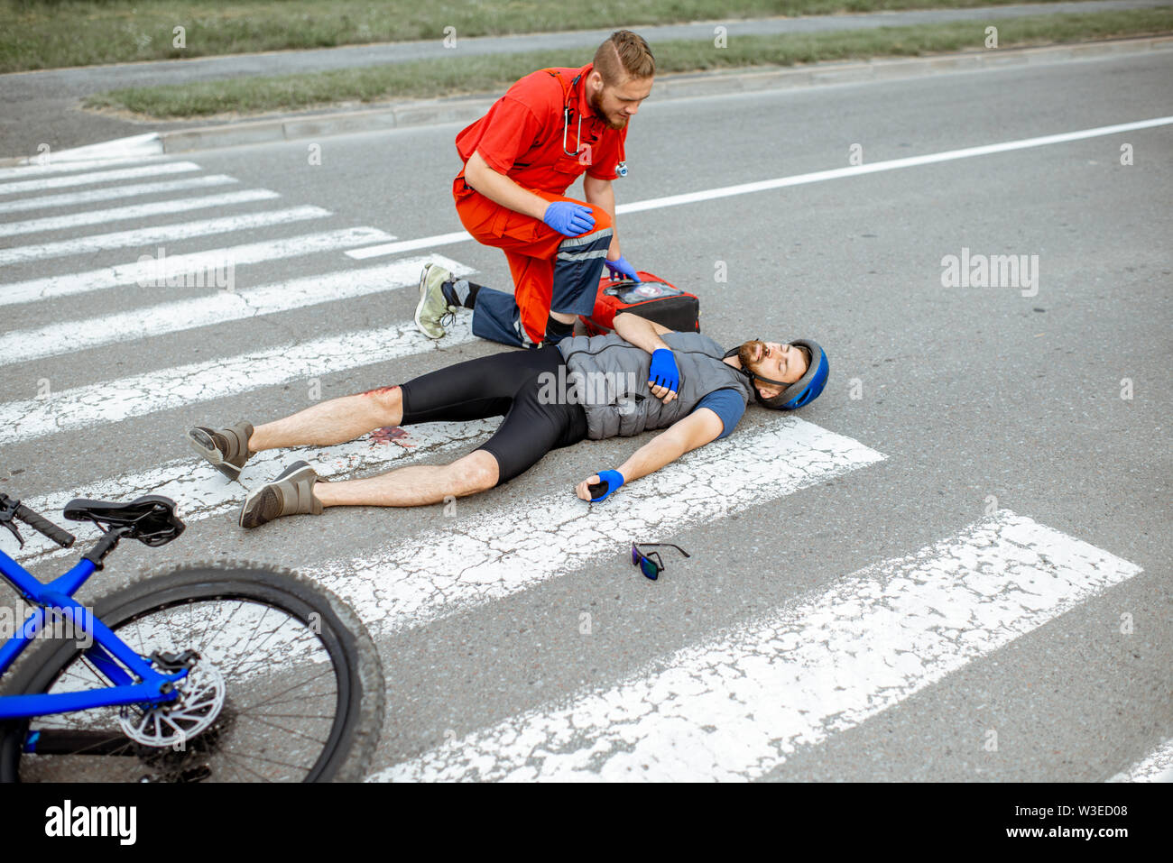 Medic applying first aid to the injured cyclist lying on the pedestrian ...