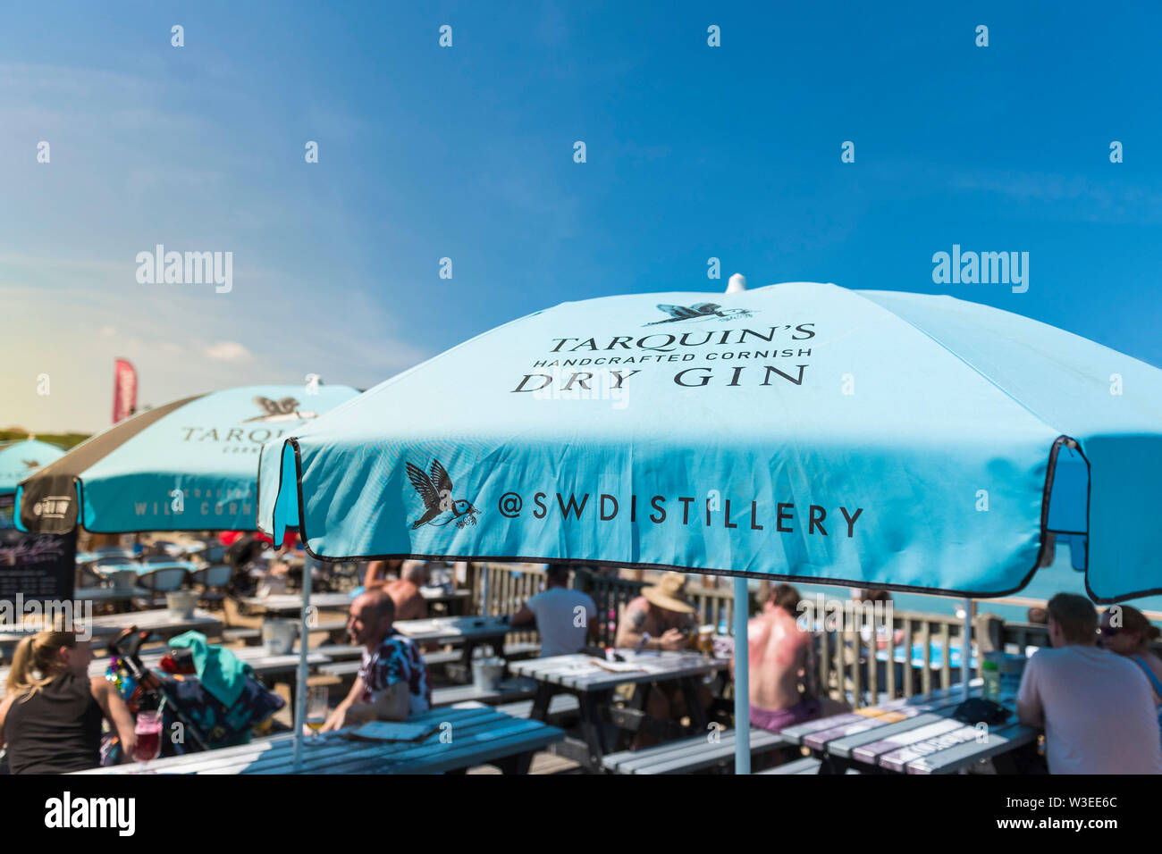 Tarquin’s Gin sponsored umbrellas providing welcome shade on a very hot day over Fistral Beach Bar in Fistral in Newquay in Cornwall. Stock Photo