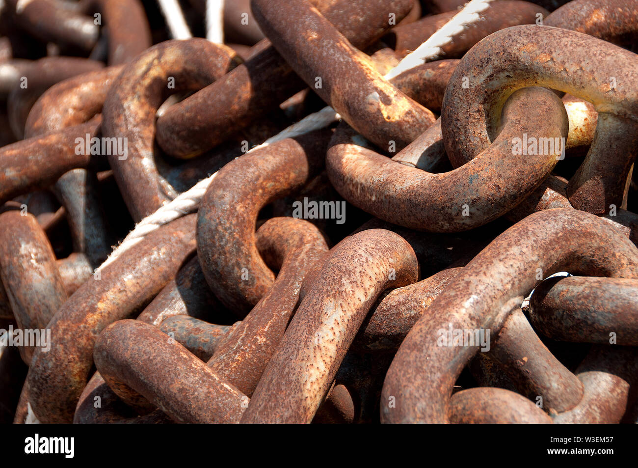 Thick, metal chain with heavy rust deposits and rope at shipyard on