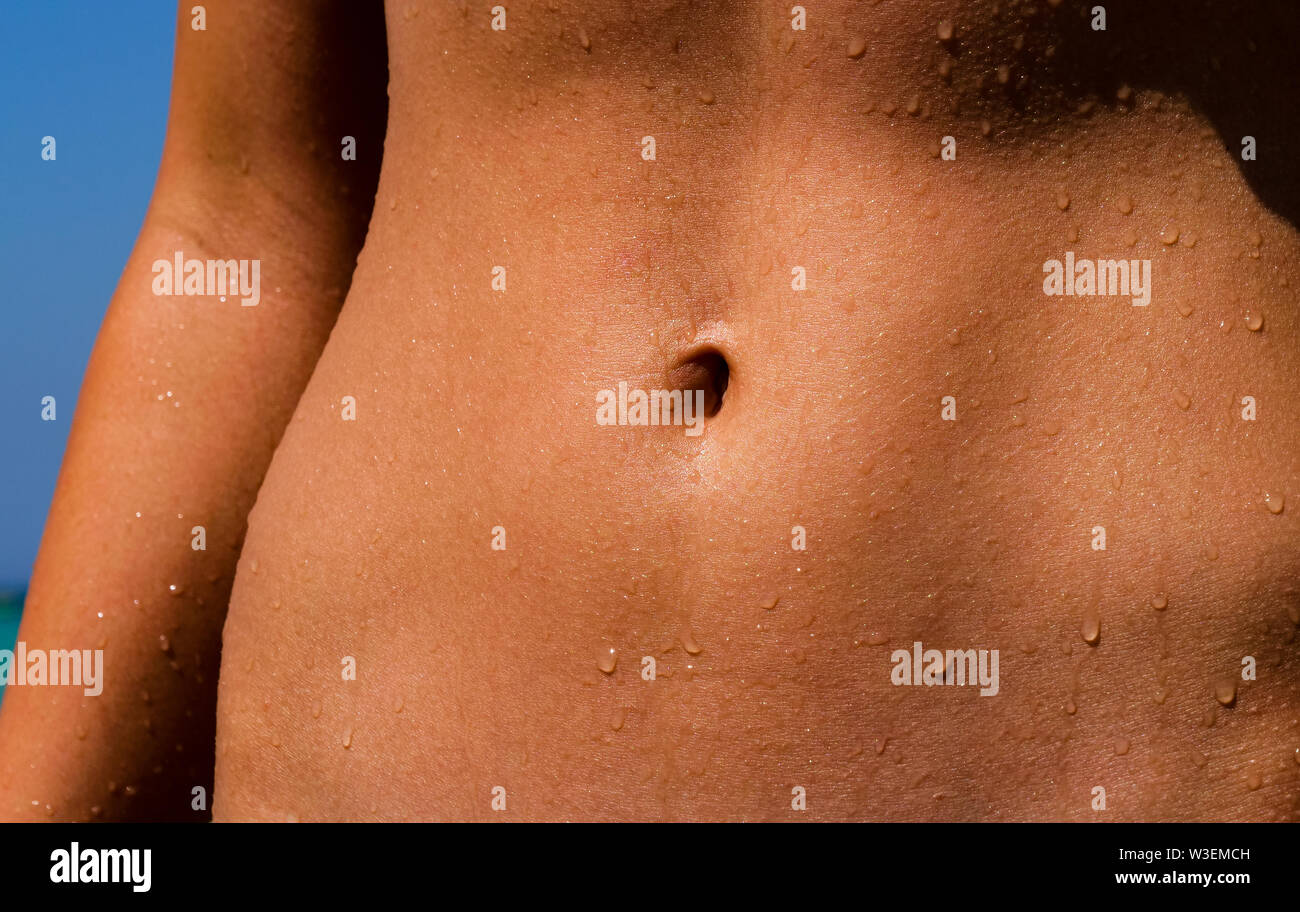 Beautiful athletic tanned body of a girl coming out of the ocean. On the belly are still some water drops from the ocean. Suitable for Fitness, Wellne Stock Photo