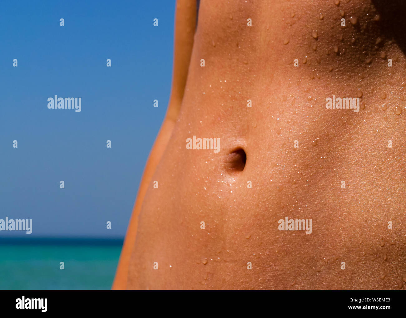 Beautiful athletic tanned body of a girl coming out of the ocean. On the belly are still some water drops from the ocean. Suitable for Fitness, Wellne Stock Photo