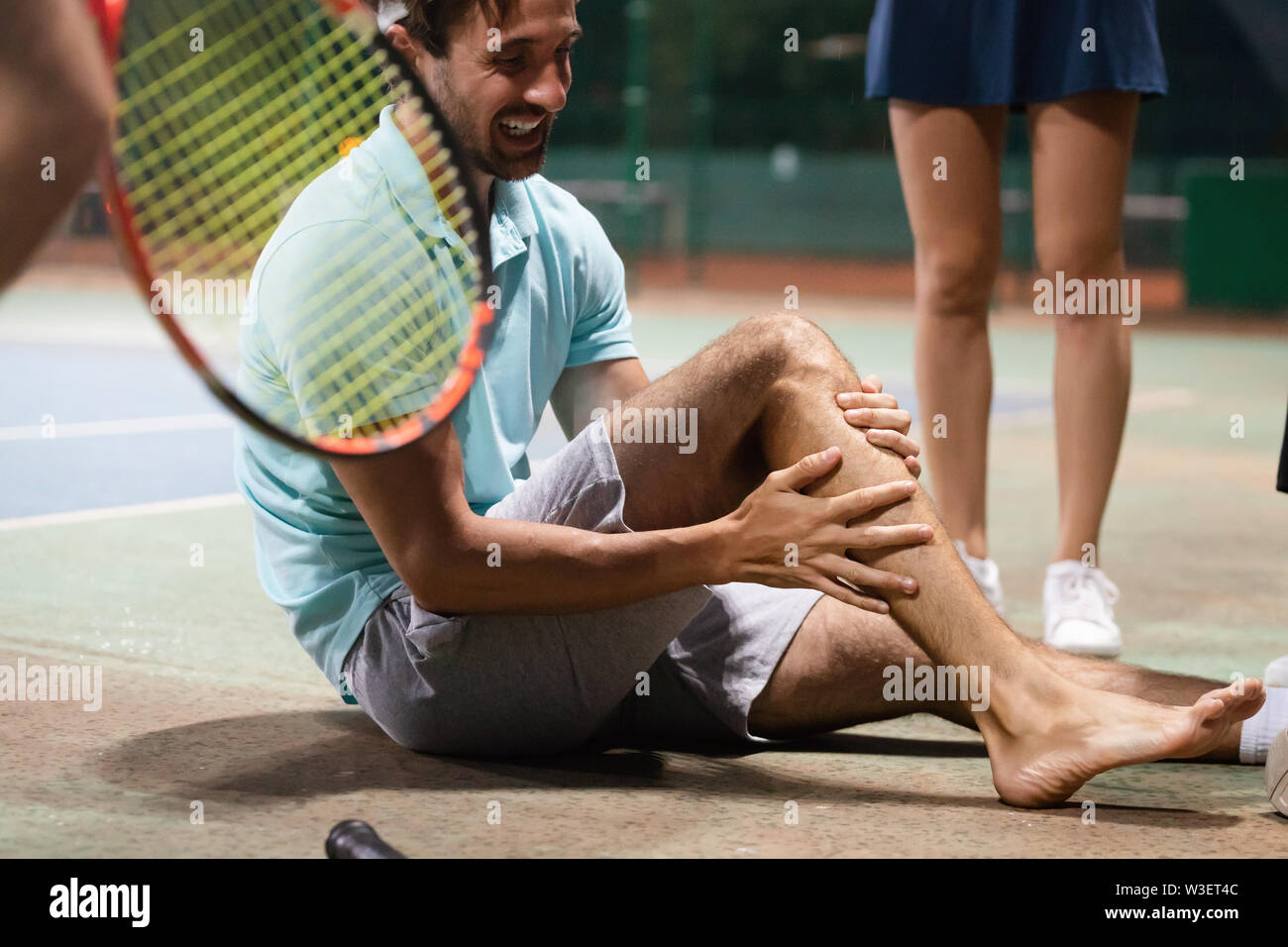Sports injury. Young tennis player touching his knee while sitting on