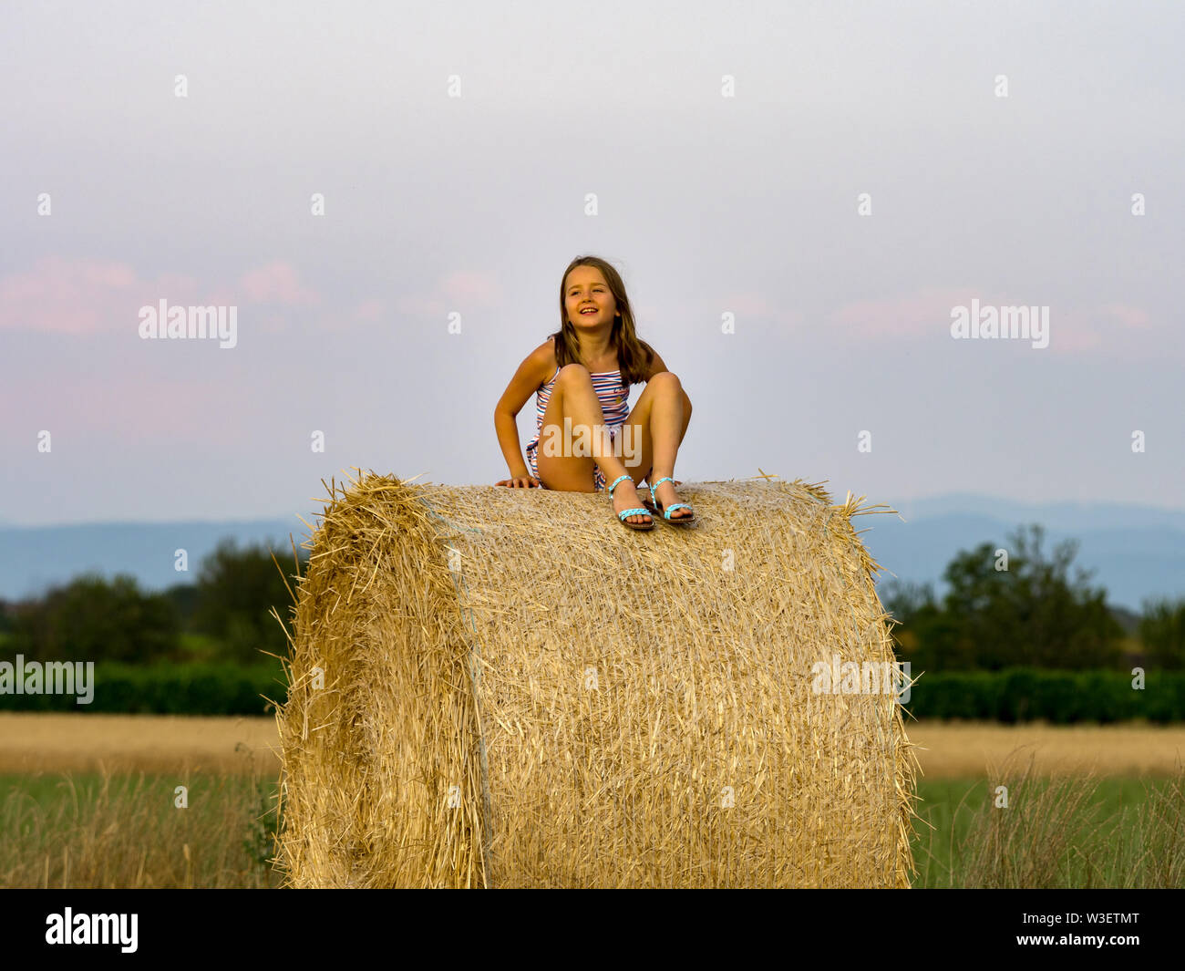 The little girl sits on a haystack in the twilight of day, Alsace ...