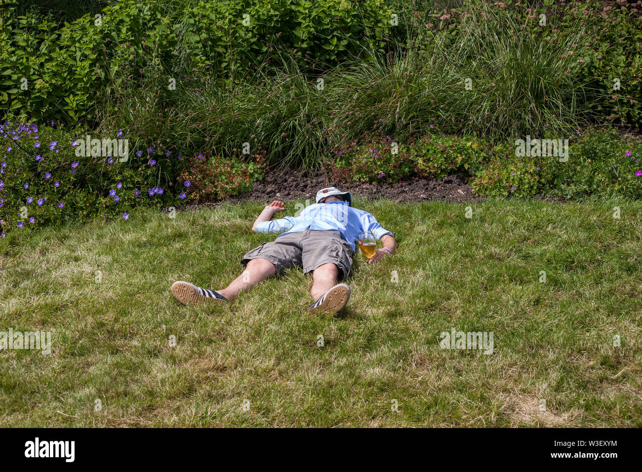 man passed out on grass bank with glass of beer in his hand at wimbledon 2019 Stock Photo