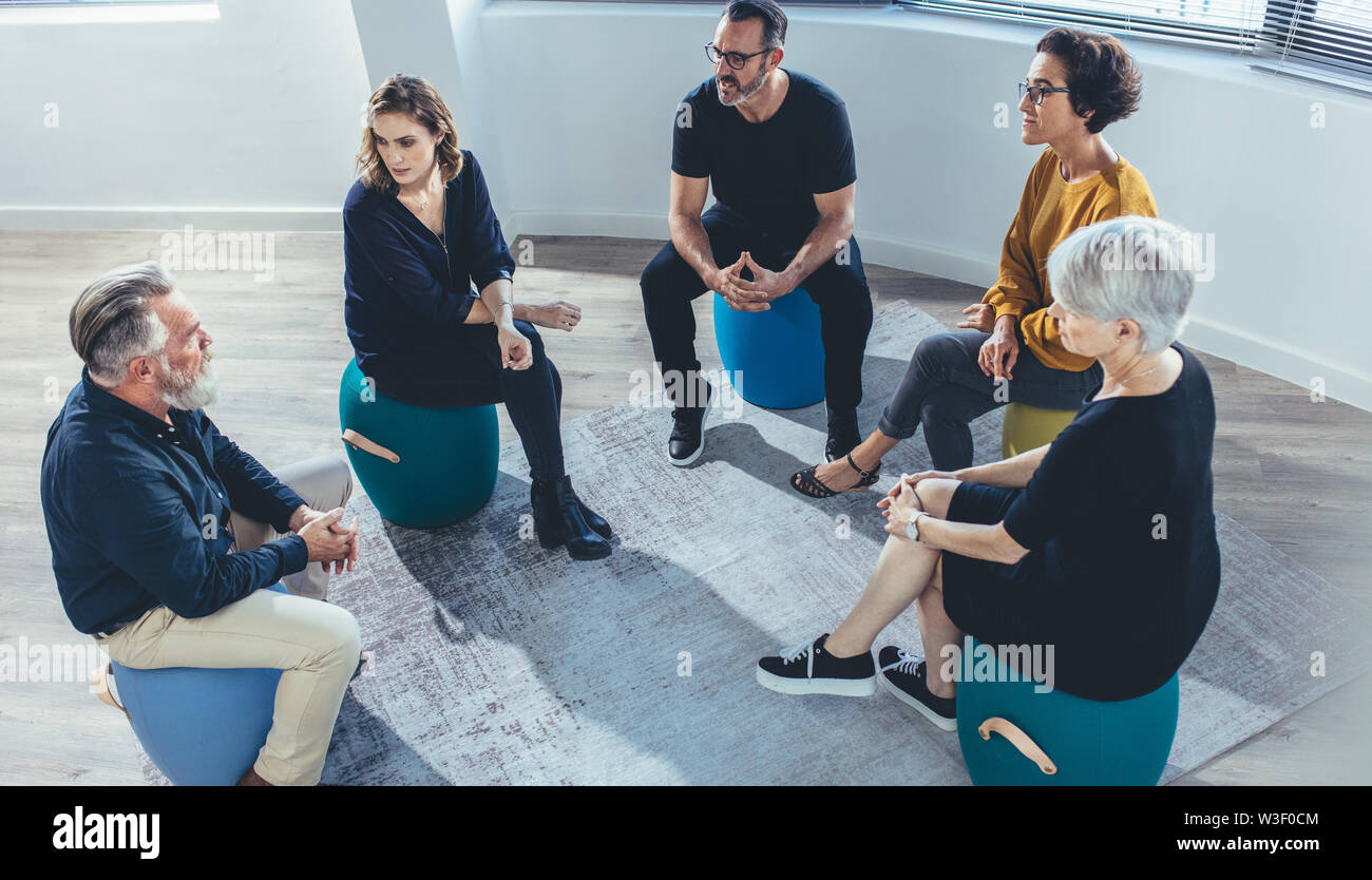 Business team sitting in circle and discussing in the office. Group of people sitting in a lesson on team building. Stock Photo