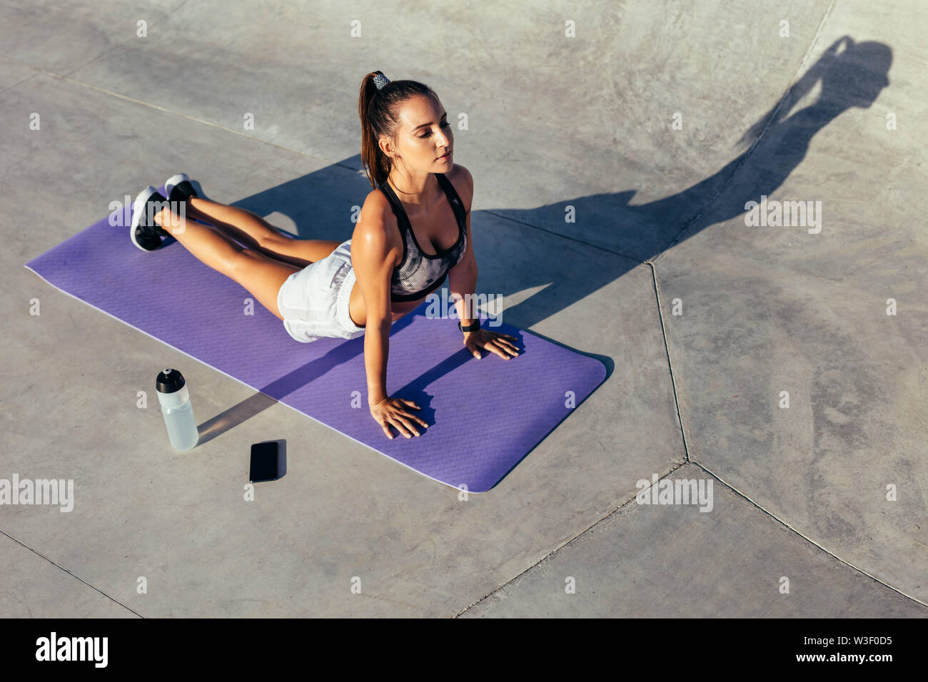 Female in sportswear practising yoga outdoors. Sporty girl doing yoga stretches workout in morning. Stock Photo