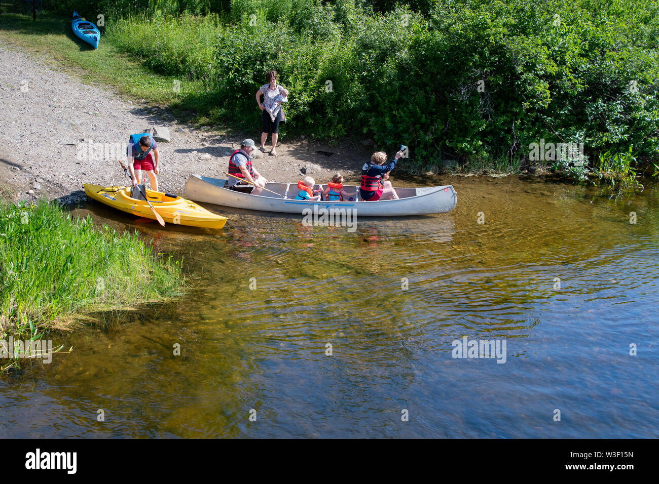 People launching a canoe and a kayak into the Sacandaga River at the outlet from Lake Pleasant in Speculator, NY USA Stock Photo