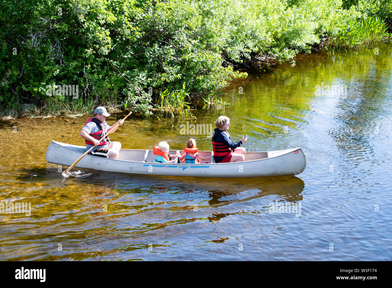 People paddling an aluminum canoe on the Sacandaga River at the outlet from Lake Pleasant in Speculator, NY USA Stock Photo