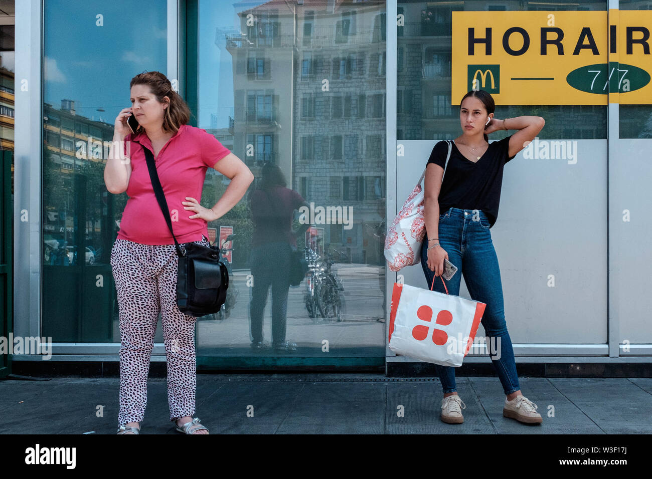 Two ladies waiting next to shop windows on a Geneva sidewalk, the young one is on her portable phone. Stock Photo