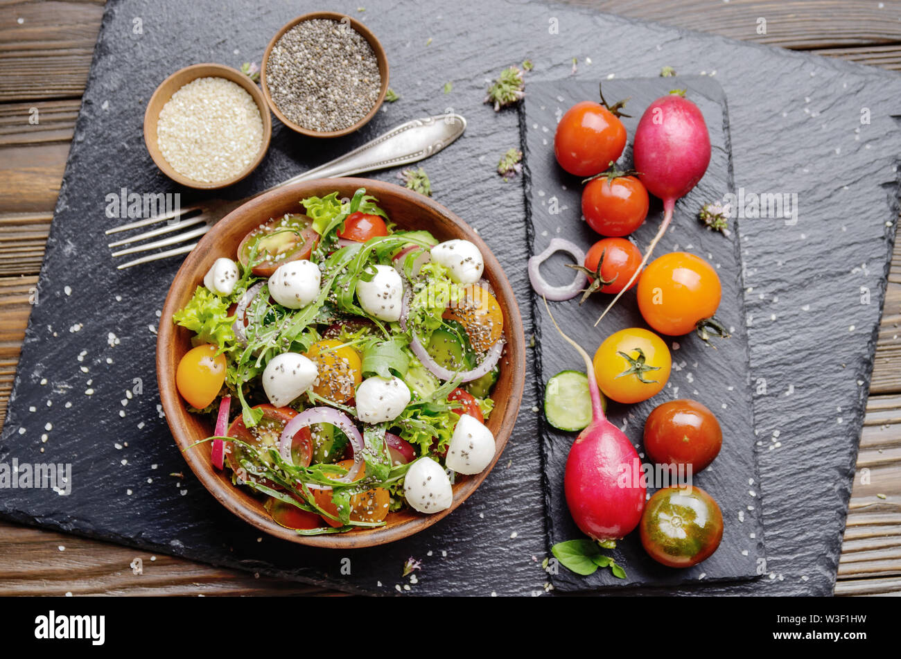 Flat lay of vegetable salad with mozzarella cheese, lettuce, cherry tomatoes, radish, cucumber, onion and basil in clay dish Stock Photo