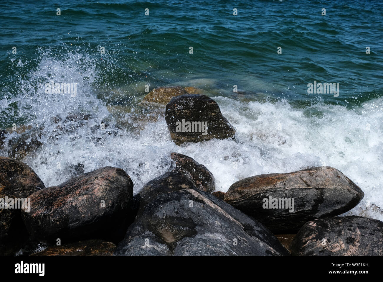 Surf foam against large rocks in blue-green water Stock Photo