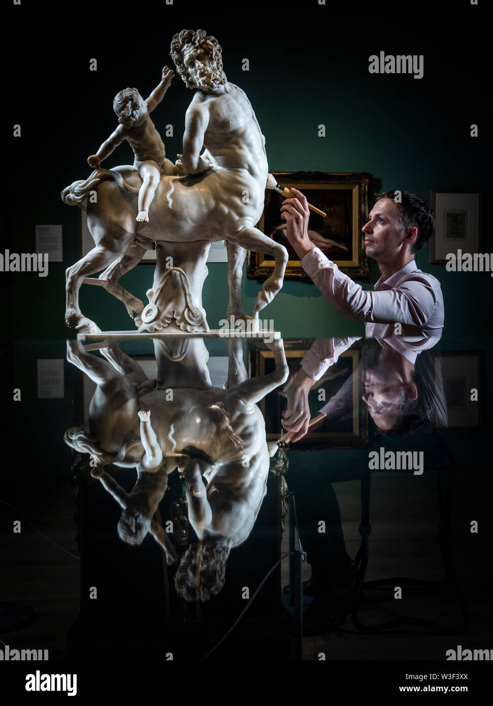 Gallery employee Lee Clark is reflected in a display cabinet, as he dusts a Old Centaur (Bound by Love) that forms part of The National Gallery Masterpiece Tour 2019, currently on show at York Art Gallery in Yorkshire. Stock Photo