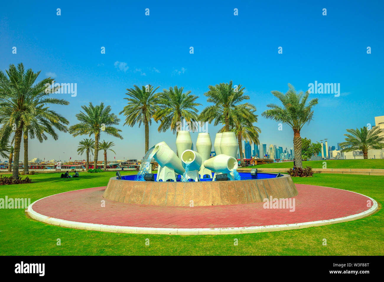 Doha, Qatar - February 16, 2019: water pots fountain or jar fountain and pal trees on Corniche promenade and Dhow Harbor with the distant business Stock Photo