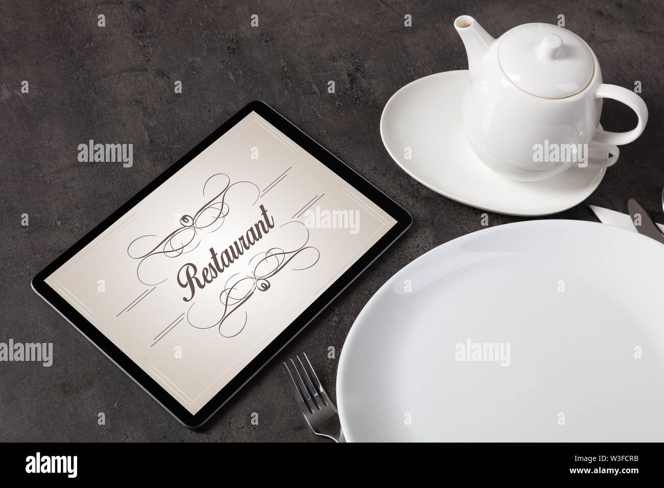 Tablet with stylish restaurant logo and laid table Stock Photo