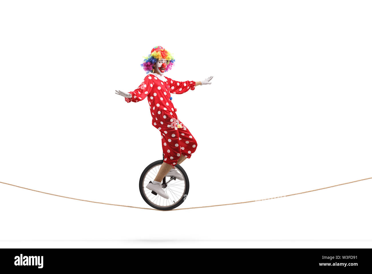 Full length profile shot of a clown riding a unicycle on a rope isolated on white background Stock Photo