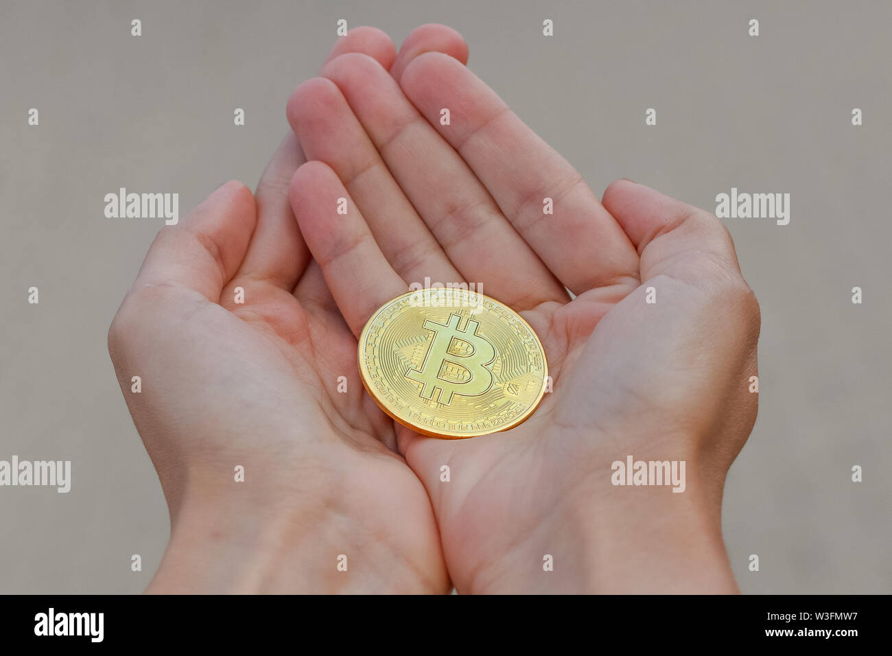 A golden cryptocurrency bitcoin coin on the elongated womens hands on a  grey background. A women hands are holding a golden big coin of bitcoin  Stock Photo - Alamy