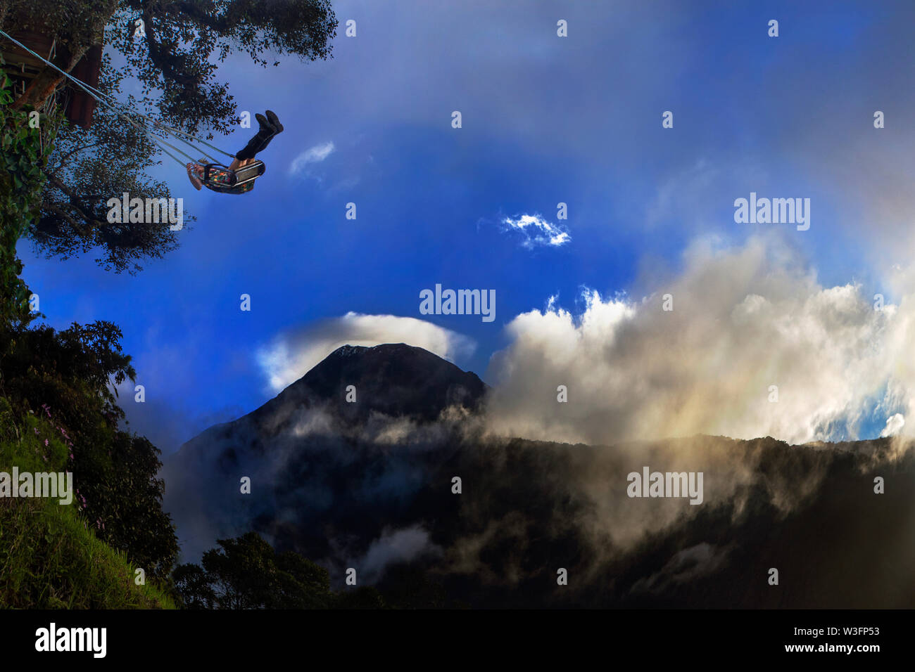 A girl enjoying on swing at the End of the World agains view of Tungurahua Volcano in beautiful Sunset Explosion Stock Photo