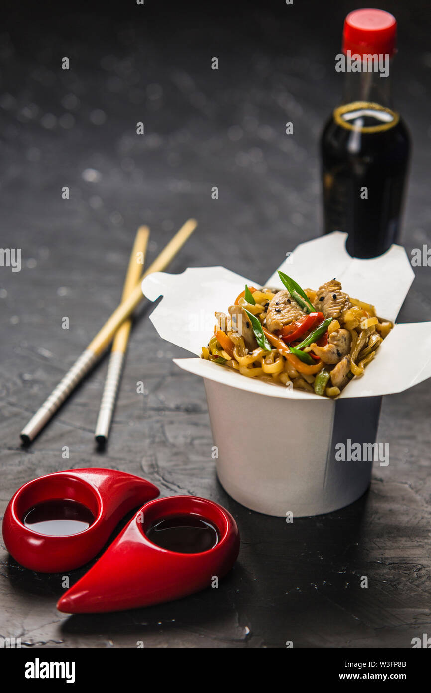 Chinese noodles in a box with chicken and vegetables with sticks. Wok