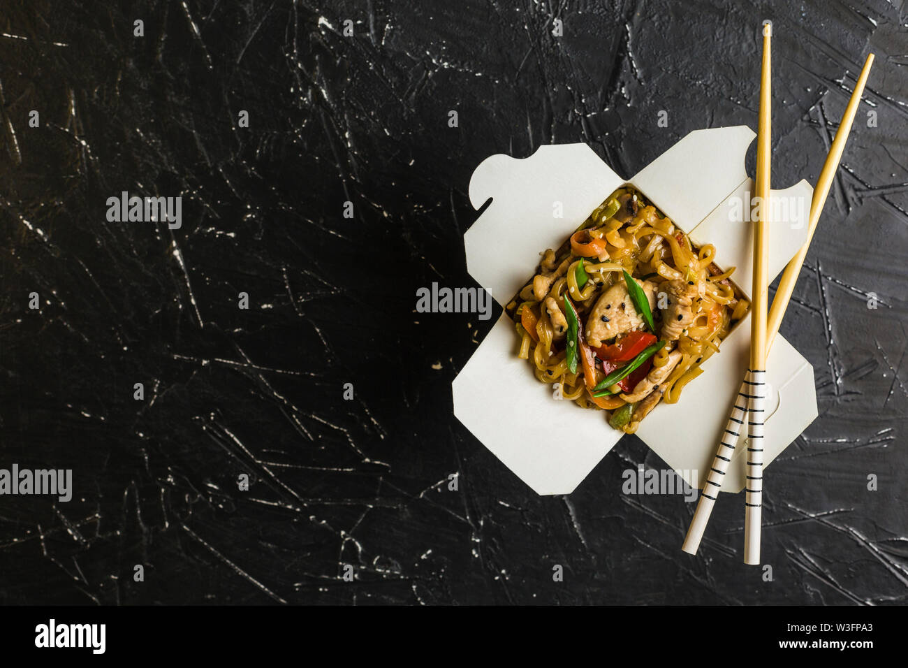 Chinese noodles in a box with chicken and vegetables with sticks. Wok