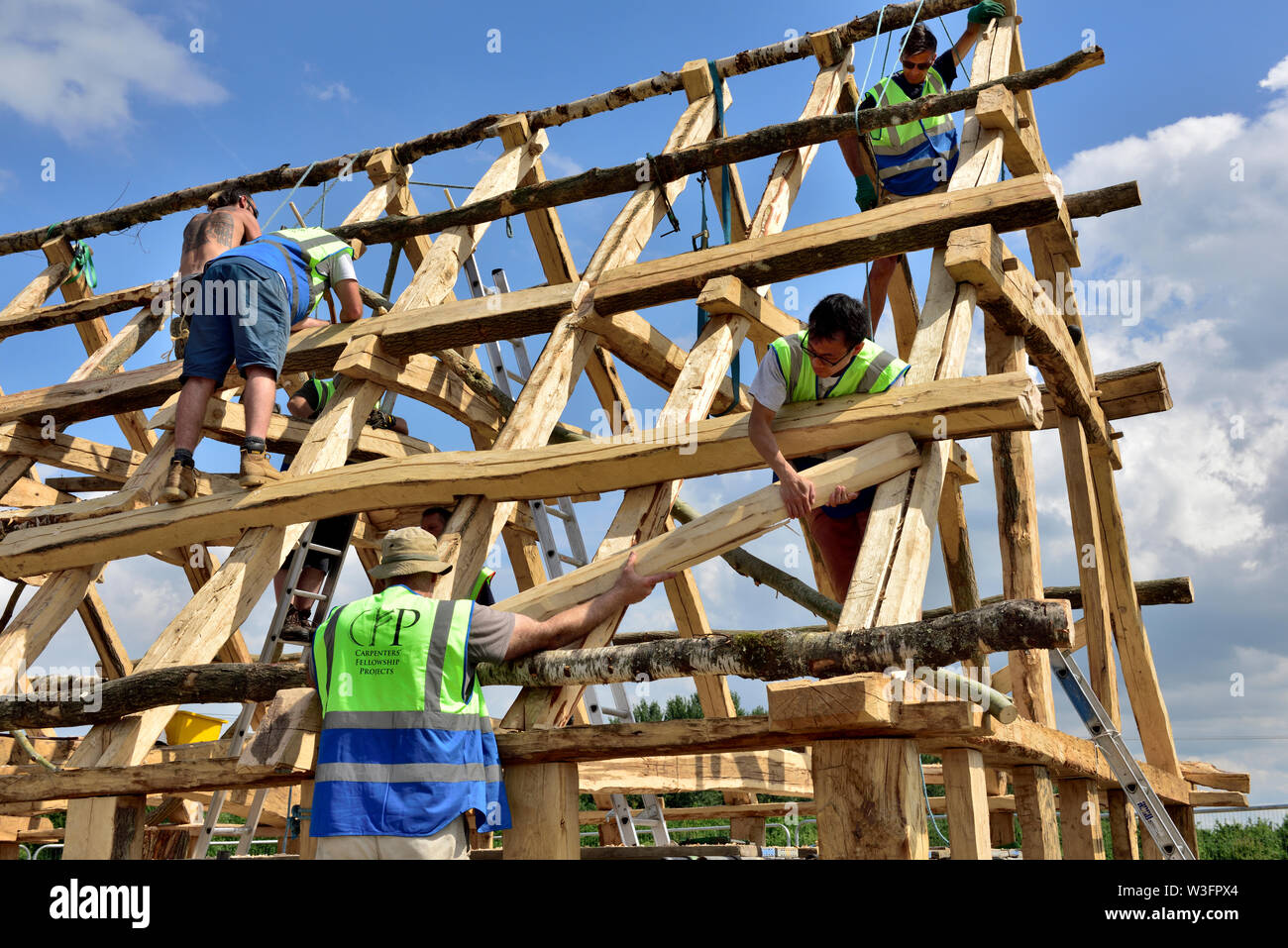 Building a traditional Anglo Saxon style heavy oak framed hall building lifting a beam up with ropes and manual handling Stock Photo