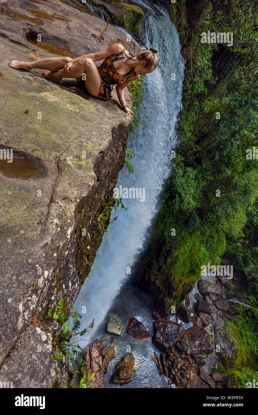 A young woman looking down the age of a cliff of Fin Del Mundo waterfall in the amazon forest of South Colombia. Stock Photo