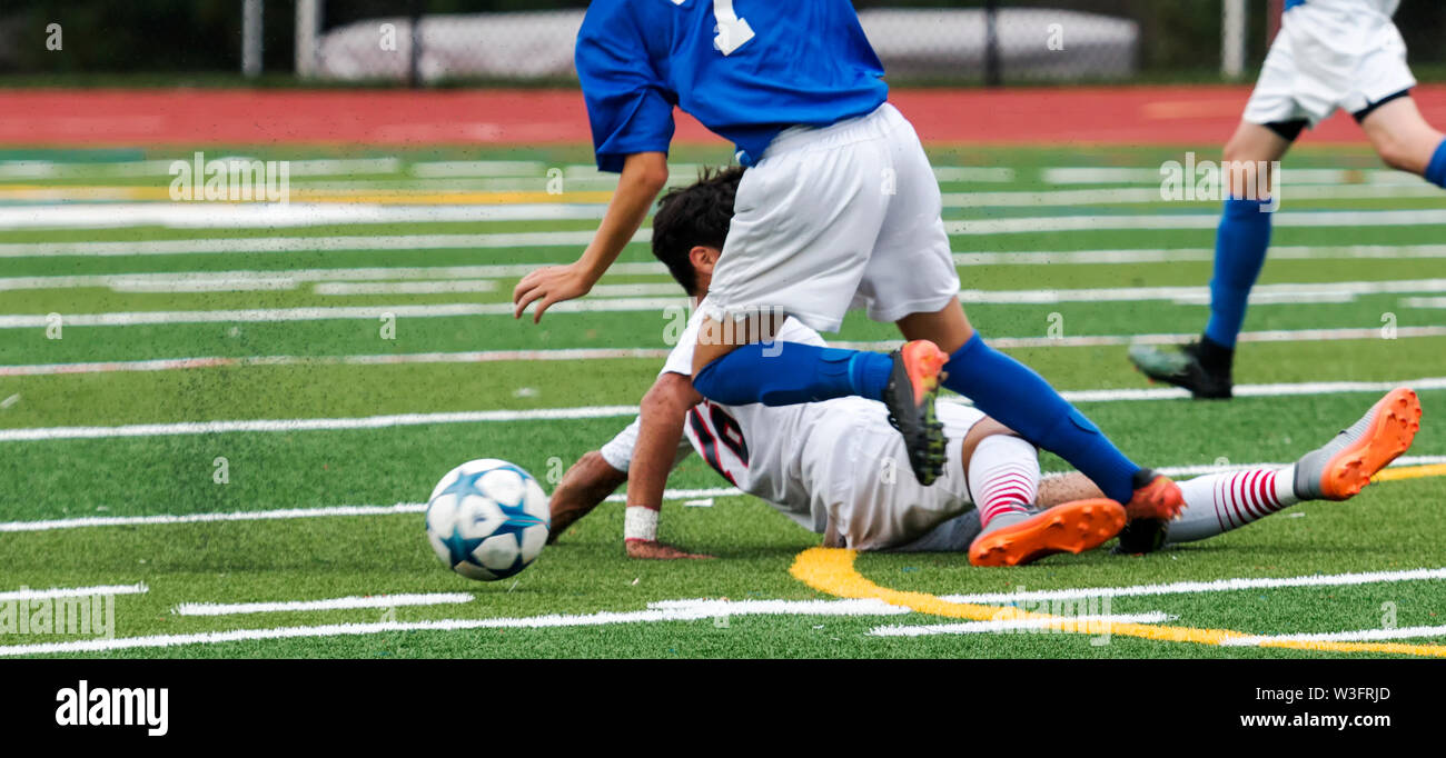 Two male soccer players fight for the ball and one slide tackles in an attempt to gain an advantage, Stock Photo