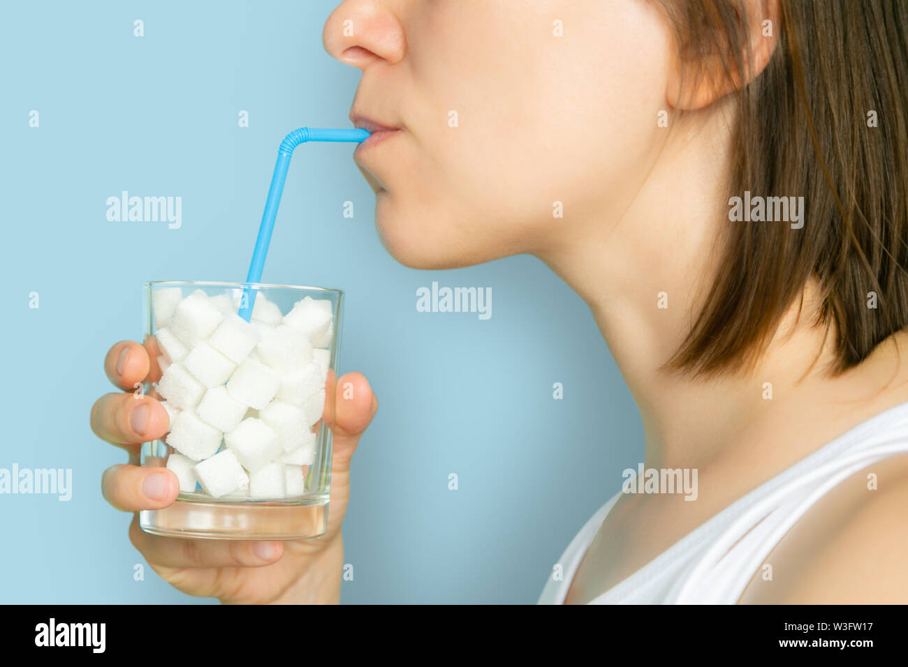 Excessive sugar consumption concept - female drinking from glass with sugar cubes Stock Photo